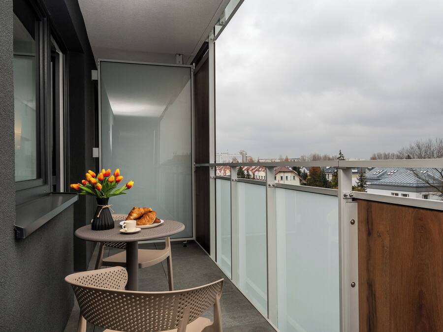Ein Balkon mit Tisch, Stühlen, einem Blumenstrauß und einem Croissant.