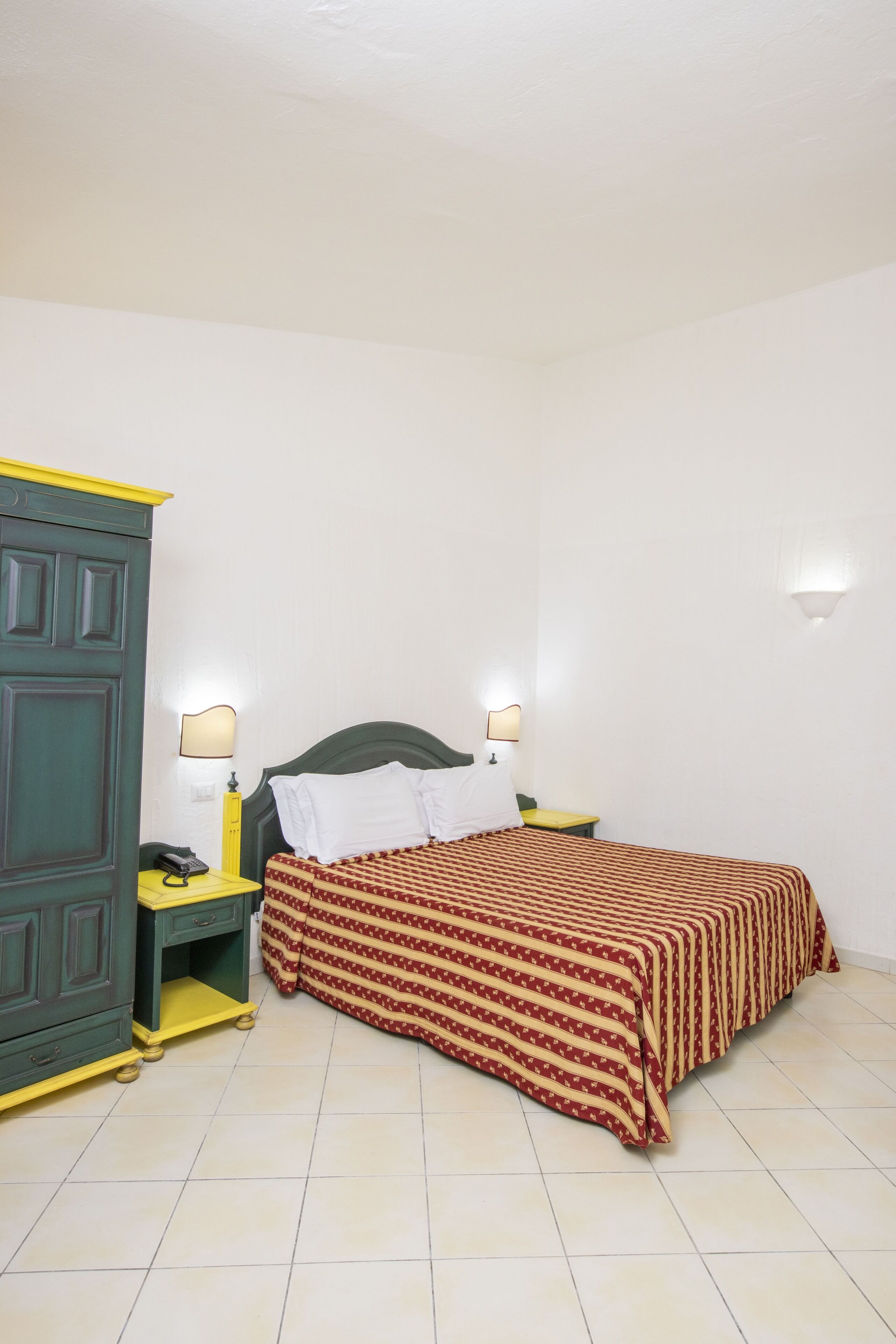 A room with a bed, two bedside tables, a wardrobe, and a lamp.
