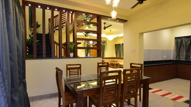 A dining area with a glass-top table, wooden chairs, a chandelier, and a ceiling fan. - SPR Paradise Resort (Vanur)