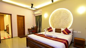 A hotel room with a large bed, a desk, a chair, a round wall light, and a ceiling fan. - SPR Paradise Resort (Vanur)