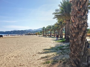 A beach with palm trees, a sandy shore, and a pier in the background. - Air-conditioned studio cabin with pool and parking in Bormes-les-Mimosas (Bormes-les-Mimosas)