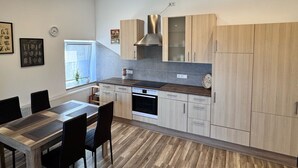 A modern kitchen with light wood cabinets, a stainless steel range hood, and a built-in oven. There is a dining table with chairs and a window with curtains. - Ostersander vacation apartment - centrally located between Ihlow, Timmel, Aurich and bathing lakes (Ihlow)