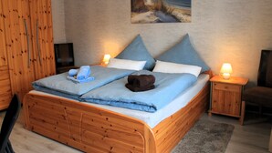 A wooden bed with a blue and white bedding, two pillows, a rolled towel, and a bedside table with a lamp. - Ostersander vacation apartment - centrally located between Ihlow, Timmel, Aurich and bathing lakes (Ihlow)