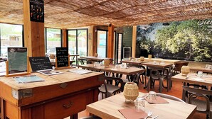 Interior rústico de restaurante con mesas y sillas de madera, una pizarra con el menú y un mural en la pared.