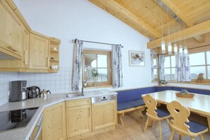 A kitchen with wooden cabinets, a sink, a coffee maker, and a dining table with chairs. - Quiet Alpine Cottage for 9 With Suana (Wald im Pinzgau)
