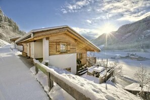 A wooden cabin with a porch, situated by a snow-covered lake, with mountains in the background. - Quiet Alpine Cottage for 9 With Suana (Wald im Pinzgau)