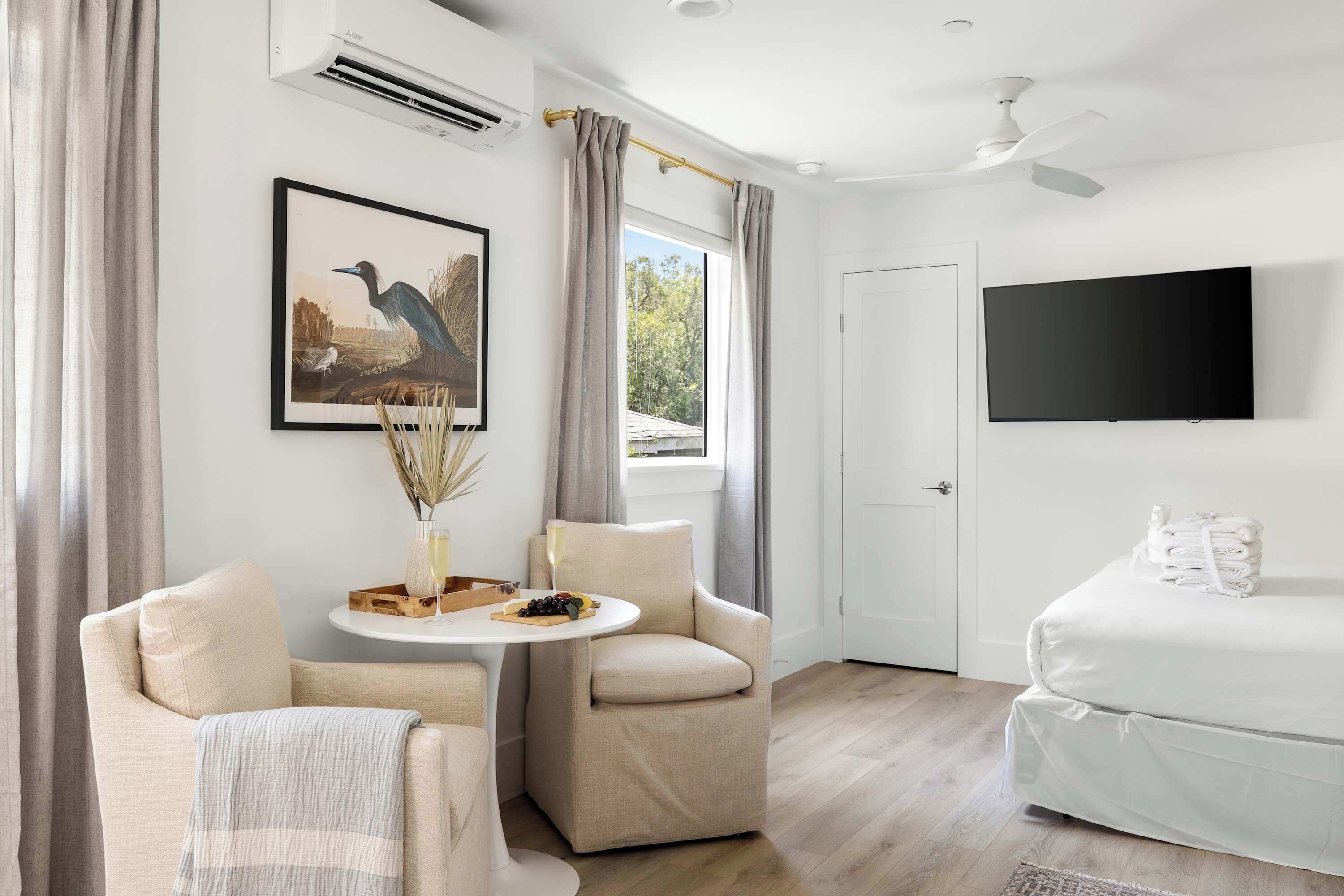Una habitación de hotel moderna con una cama, dos sillones, una mesita con un jarrón y un televisor de pantalla plana.