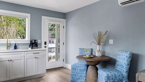 A modern kitchen with white cabinets, a coffee machine, and a dining area with patterned chairs and a round table. - Beautiful Studio with Kitchen + Parking (Folly Beach)