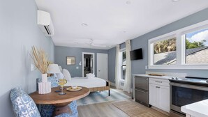 A modern bedroom with a bed, bedside table, and a window. - Beautiful Studio with Kitchen + Parking (Folly Beach)