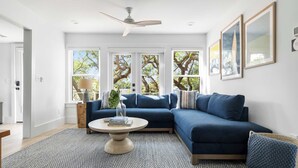 Ein modernes Wohnzimmer mit einem blauen Ecksofa, einem runden Couchtisch und einem Deckenventilator.