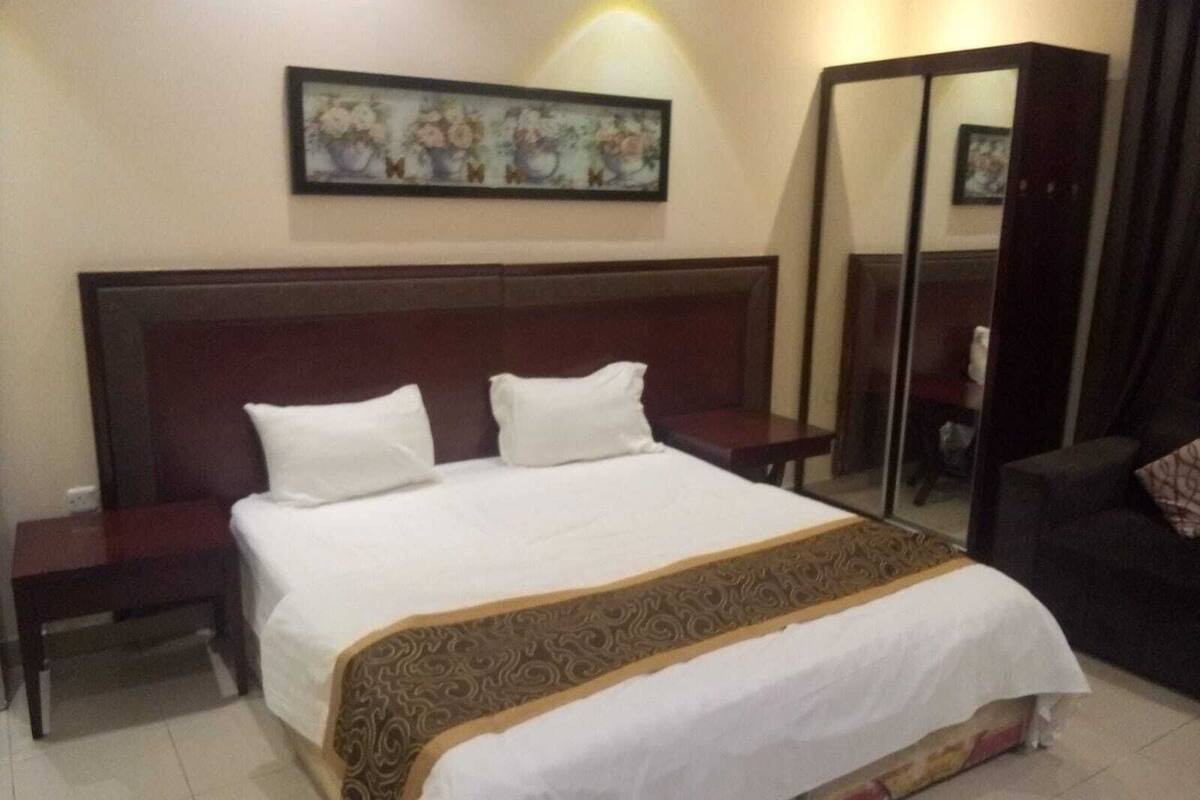 Une chambre d’hôtel avec un grand lit, une table de chevet, une commode, un miroir et un tableau au mur.
