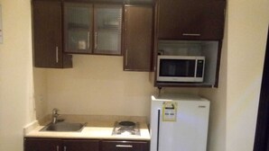 Una cocina compacta con armarios marrón oscuro, encimera blanca, microondas y refrigerador.