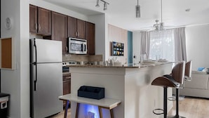 A modern kitchen with dark wooden cabinets, stainless steel appliances, and a central island with bar stools. - Dallashaus Near Galleria Medical City (Dallas)
