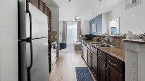 A modern kitchen with a refrigerator, oven, and sink. There is a ceiling fan and a window with curtains. - Dallashaus Near Galleria Medical City (Dallas)