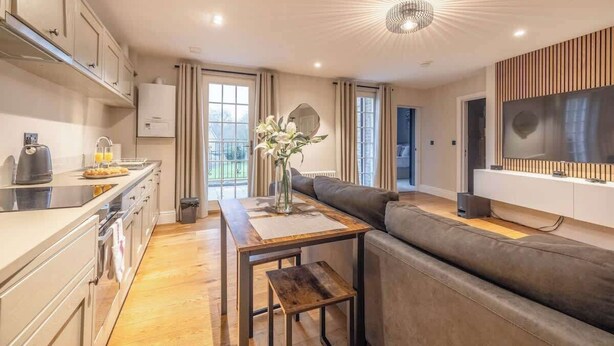 A modern kitchen with a dining area, a sofa, and a TV.