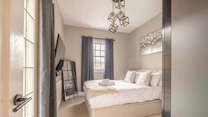 A bedroom with a bed, a window with curtains, a wall-mounted artwork, and a ceiling light fixture.
