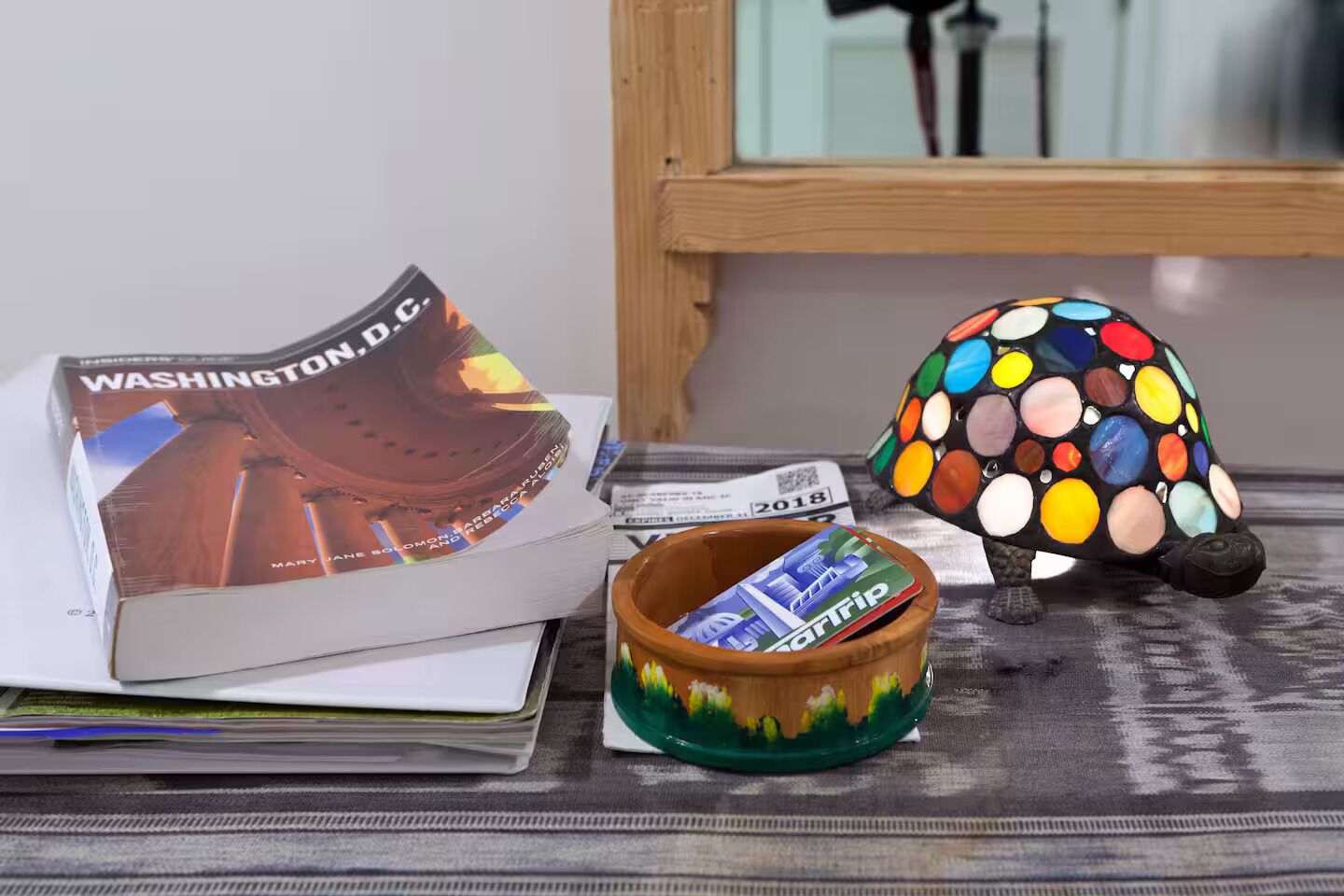 Un libro intitolato 'Washington D.C.', una colorata tartaruga in ceramica e una piccola ciotola con un motivo che raffigura un paesaggio verde.