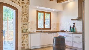 Una cocina con armarios blancos, un barril de madera y una ventana con vistas a follaje.