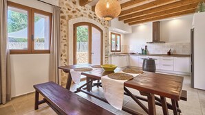 Una cocina rústica con vigas de madera, una mesa de comedor con individuales y un ventanal con cortinas.