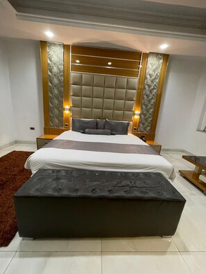 Un dormitorio moderno con una cama grande, un cabecero capitonado y un otoman oscuro.