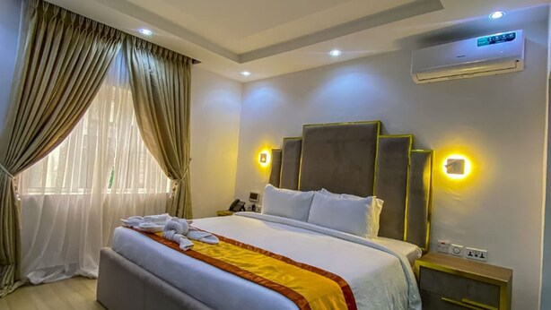 Una habitación de hotel moderna con una cama grande, una mesita de noche, un aire acondicionado y una ventana con cortinas.