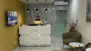 Una zona de recepción moderna con suelo de mármol, un mostrador de recepción, un televisor y una lámpara en el techo.