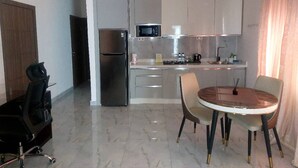 Cocina compacta con refrigerador, microondas y estufa. Hay una mesa de comedor con sillas y una pequeña silla de escritorio.