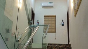 Una escalera con barandillas de vidrio y piso de mármol, que conduce a un rellano con una lámpara en el techo.