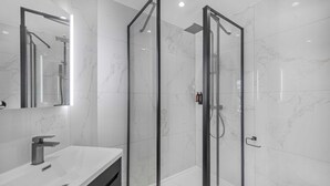 Un baño moderno con ducha de vidrio, lavamanos blanco y retrete.