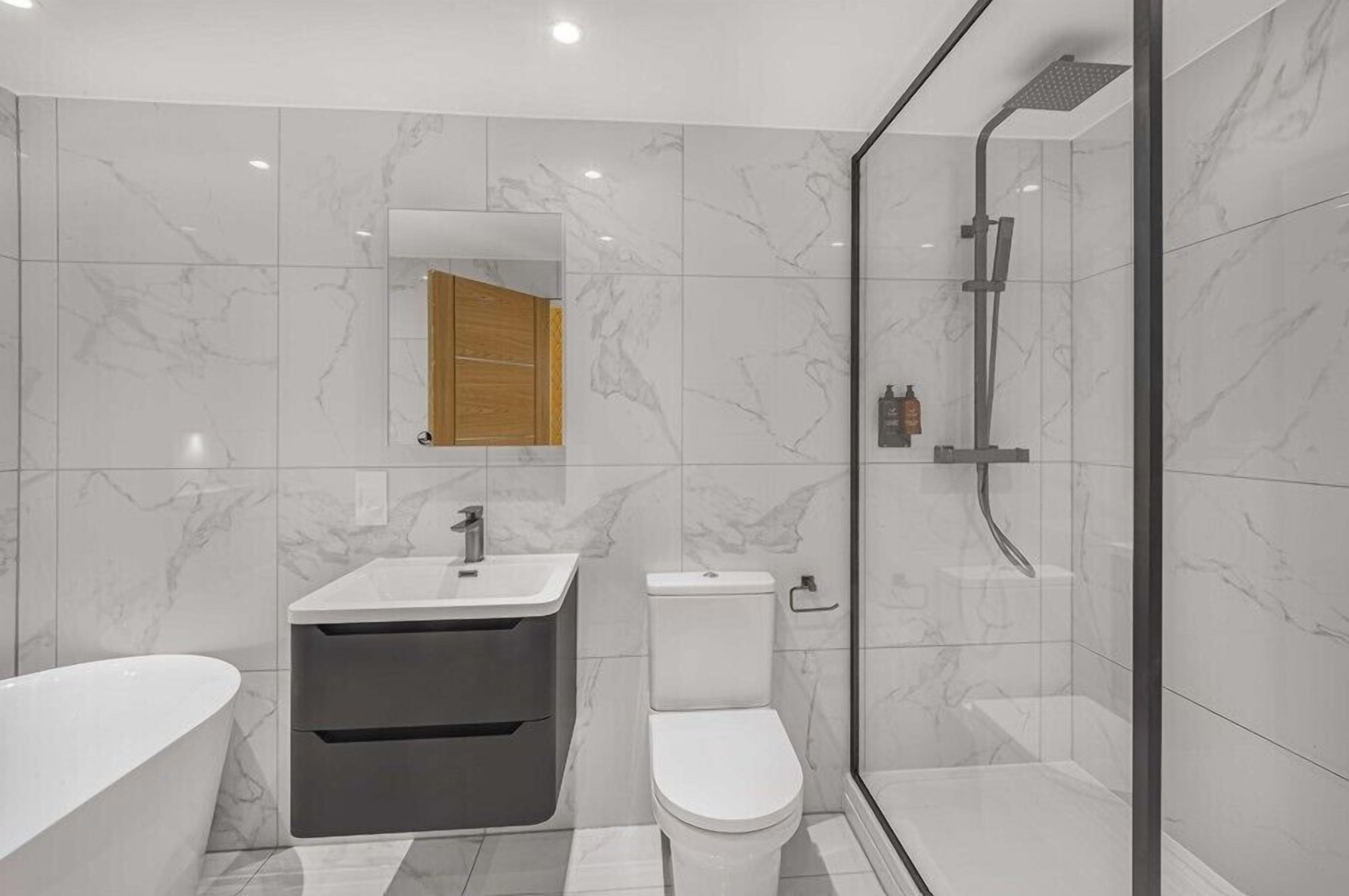 Un baño moderno con suelo de mármol, una bañera independiente, un inodoro y una zona de ducha con paredes de vidrio.