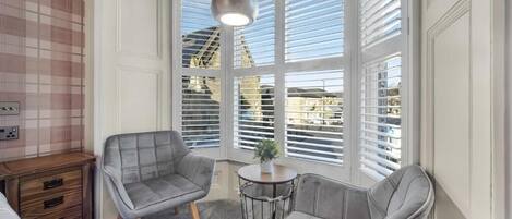 Una habitación con dos sillones grises, una mesita redonda con una planta y una lámpara colgante.