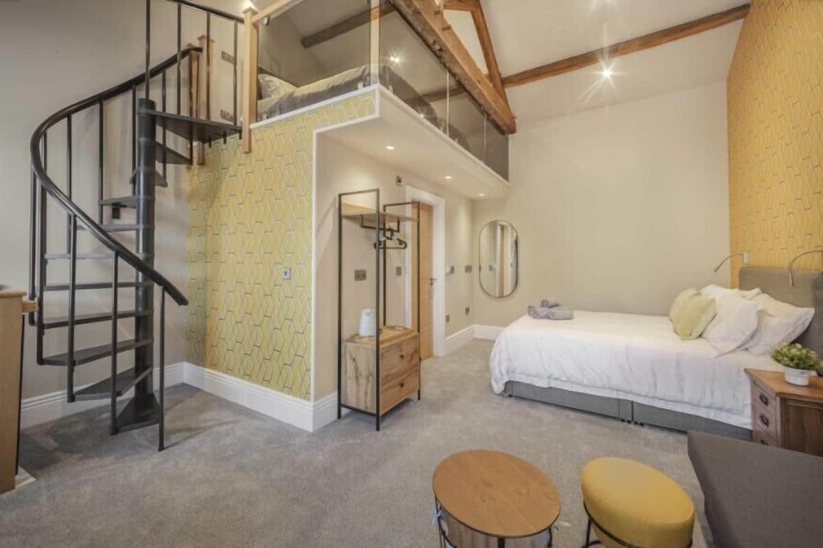 A bedroom with a bed, a small table, a chair, a staircase, and a bathroom.