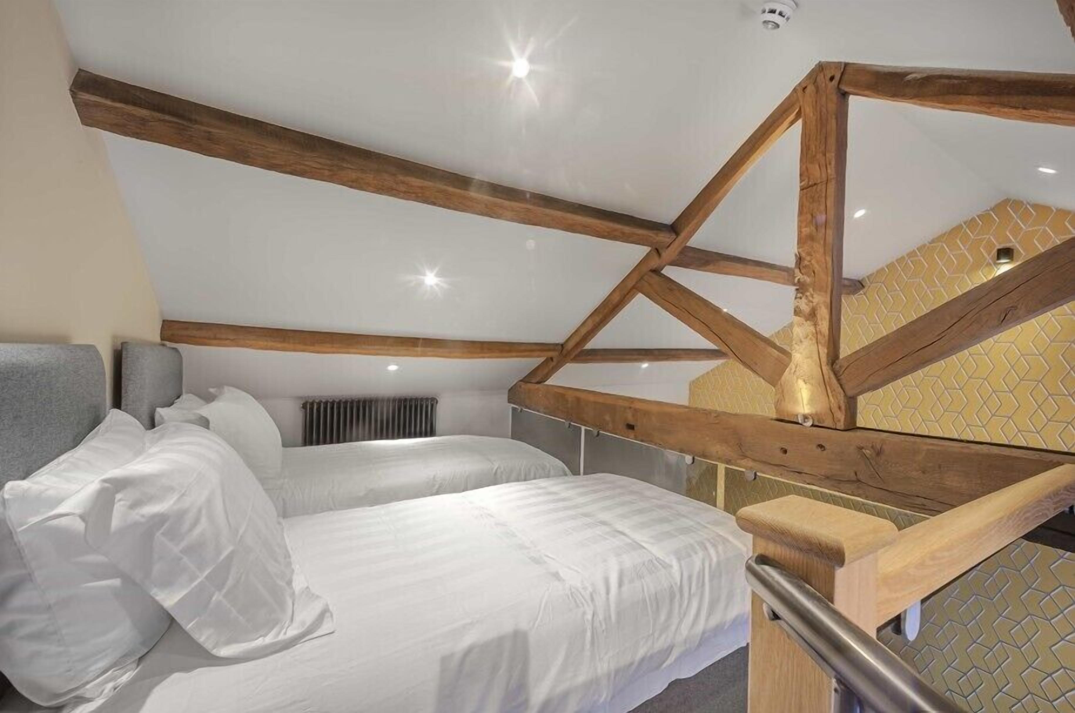 Quarto com duas camas, vigas de madeira, radiador e parede estampada.