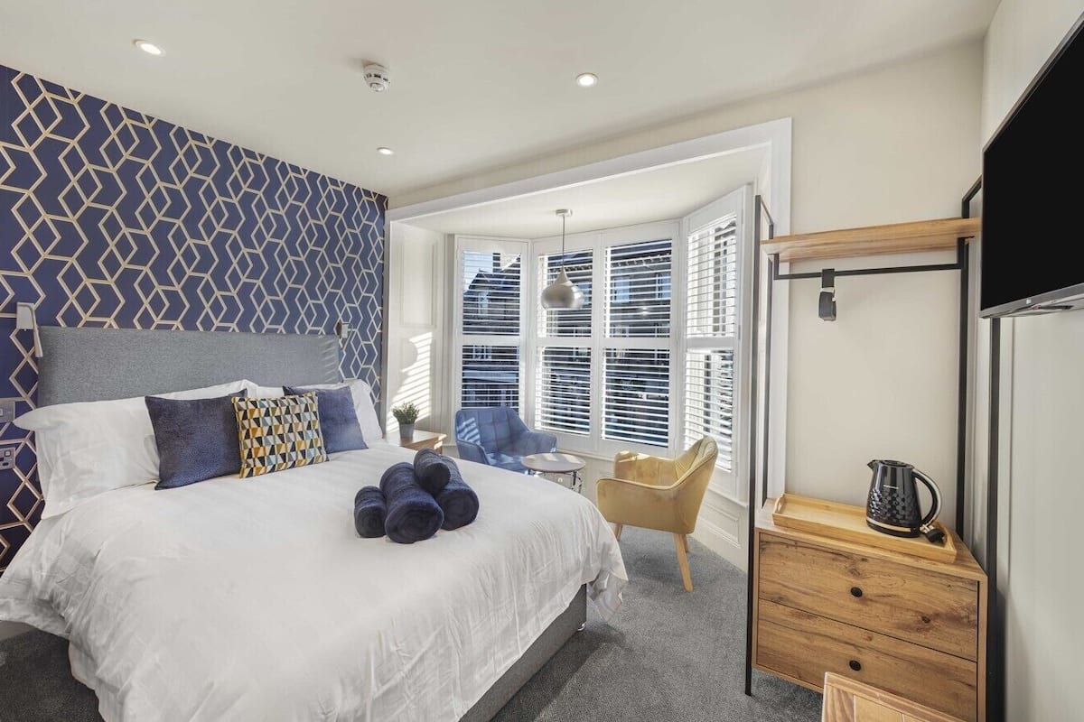 A modern bedroom with a large bed, a TV, and a window with blinds.