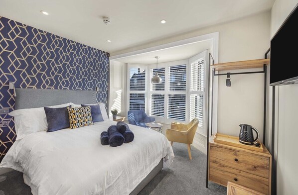 A modern bedroom with a large bed, a TV, and a window with blinds.