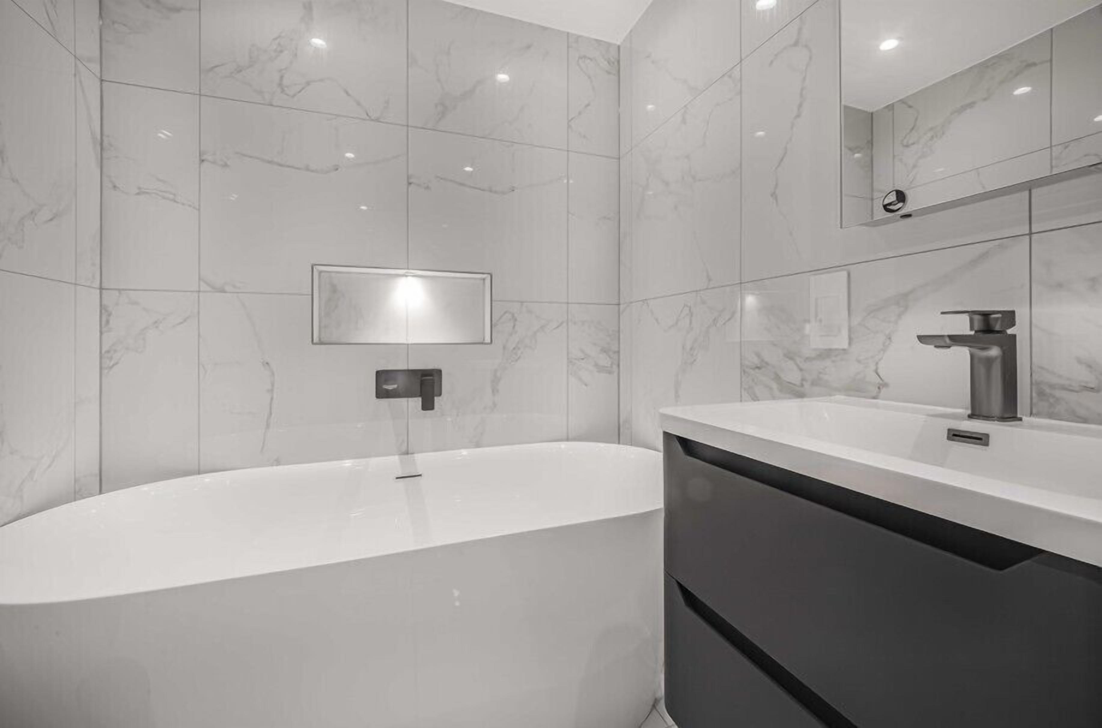 Un baño moderno con una bañera independiente, un espejo instalado en la pared y un mueble de tocador elegante.