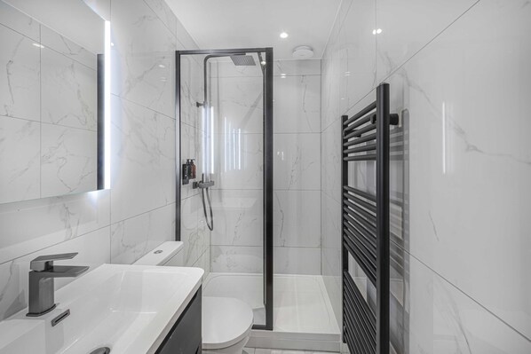 A modern bathroom with a glass-enclosed shower, a white sink, and a toilet.
