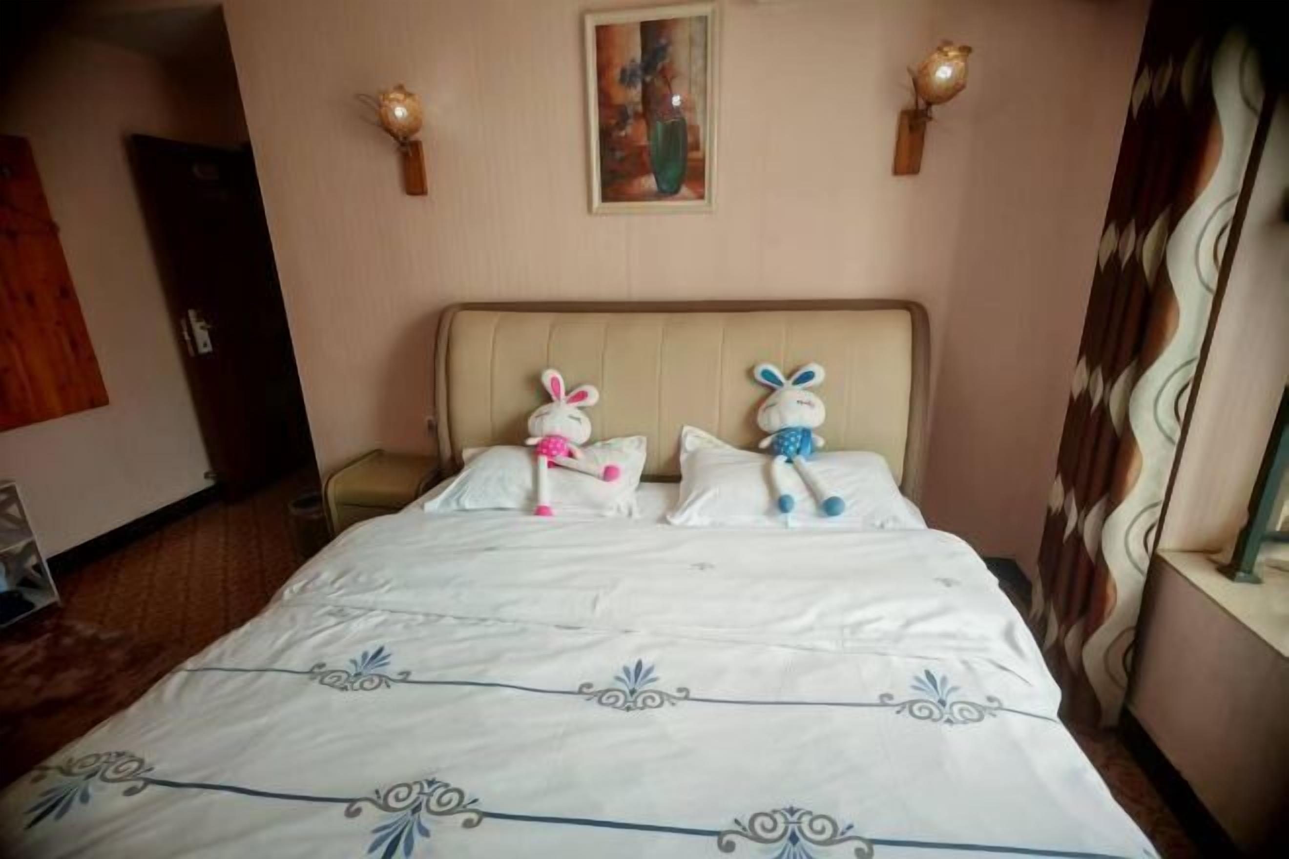 A hotel room with a bed, two wall-mounted lamps, and a painting above the bed.