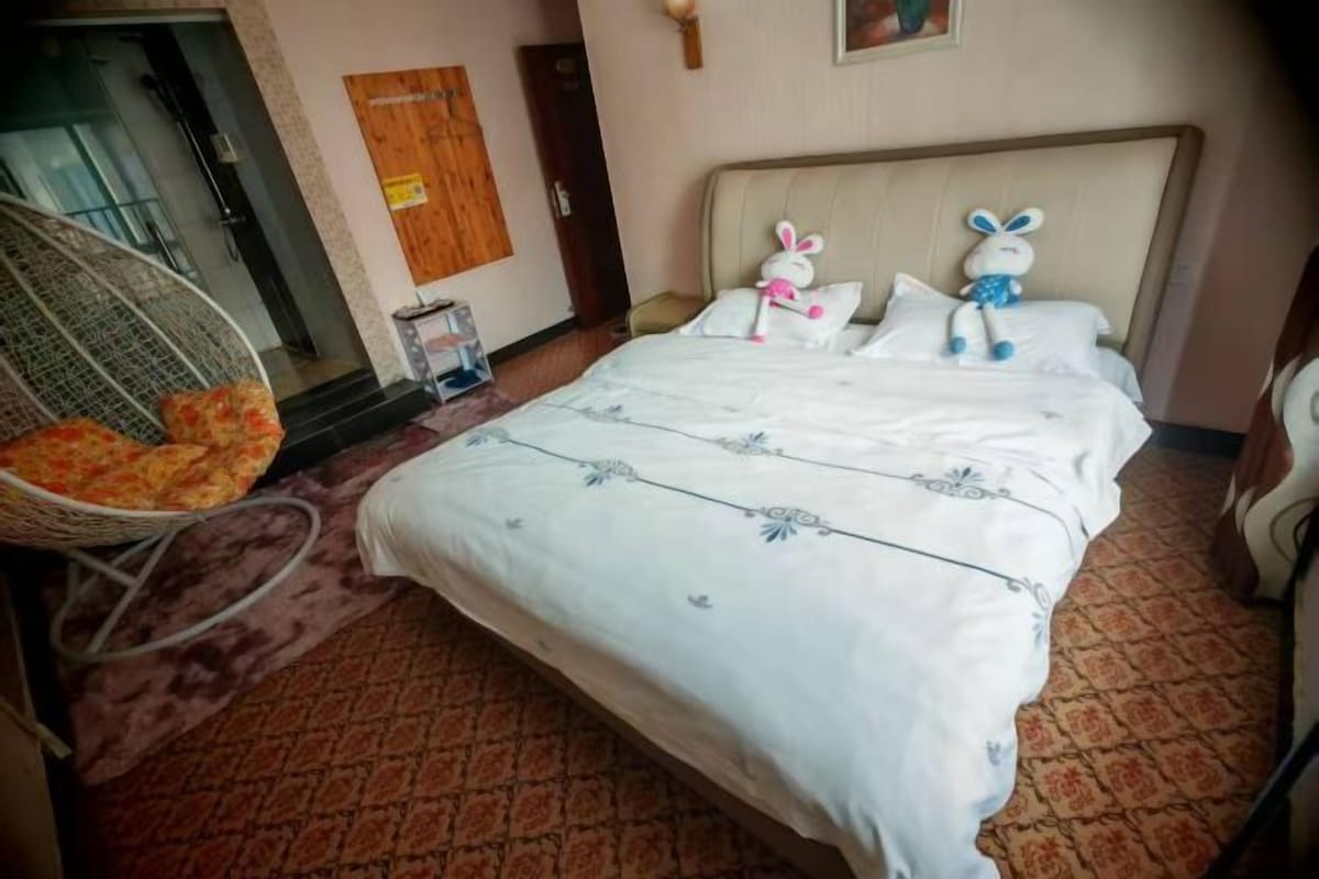 A hotel room with a bed, a wicker chair, and a small table with a basket.