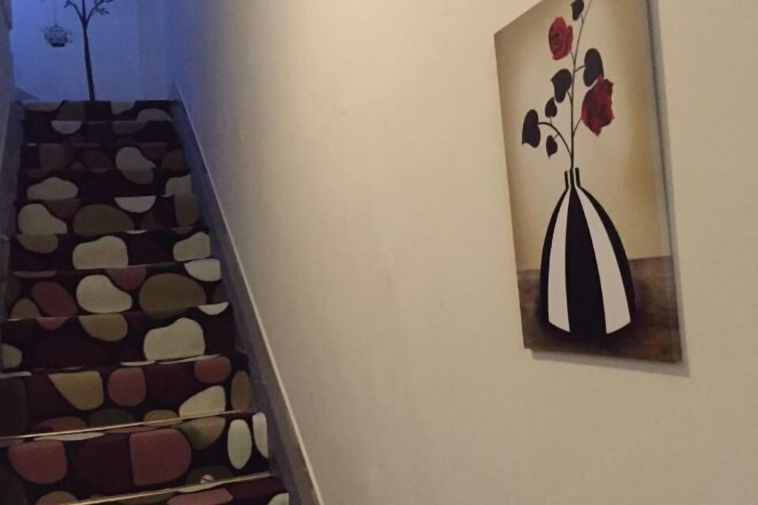 A staircase with a unique design, a wall-mounted painting of a vase with flowers, and a tree silhouette in the background.