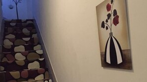 A staircase with a unique design, a wall-mounted painting of a vase with flowers, and a tree silhouette in the background.