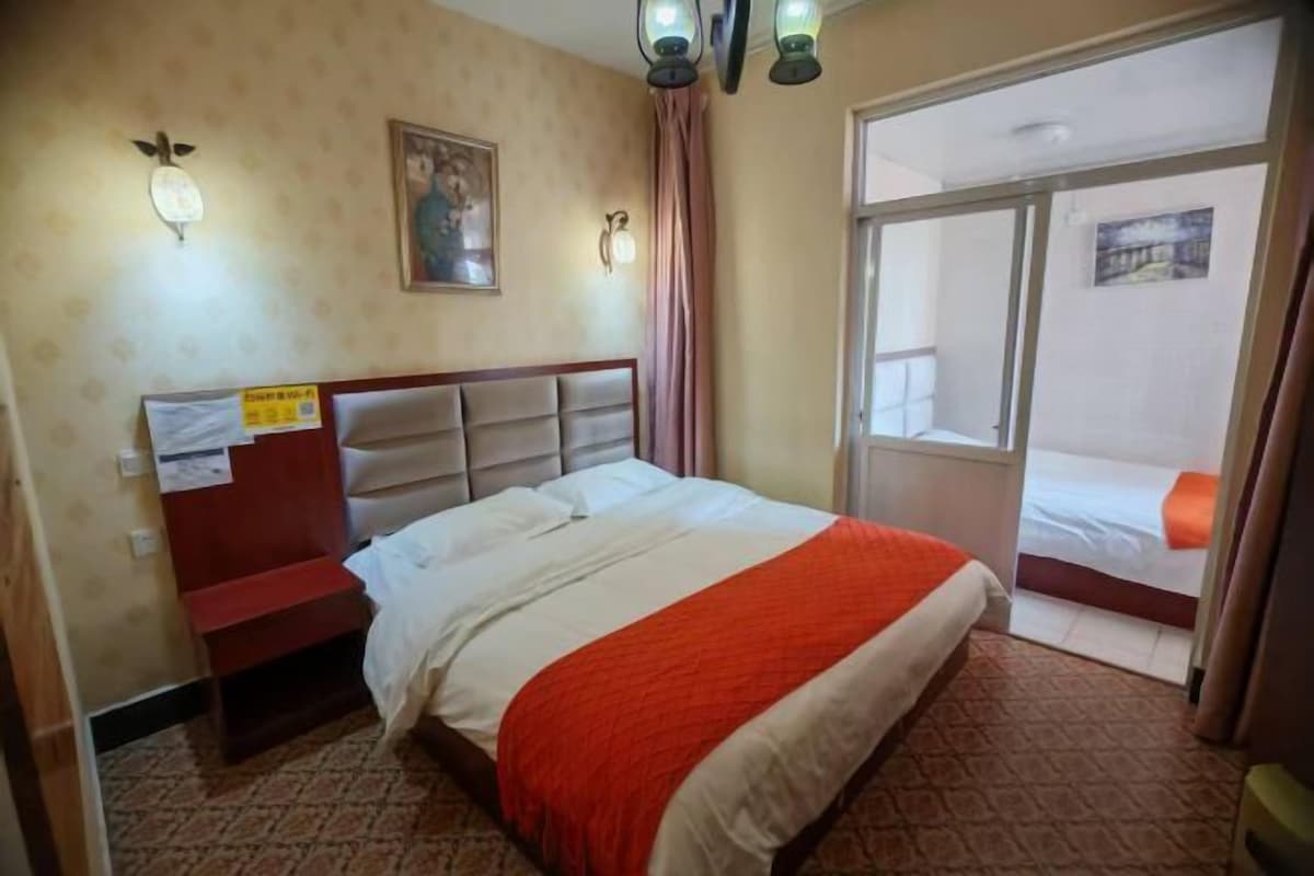 A hotel room with a bed, a desk, a chair, a window, and a door leading to a balcony.