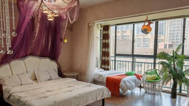 A bedroom with a large bed, a smaller bed, a window with curtains, a hanging light fixture, and a potted plant.