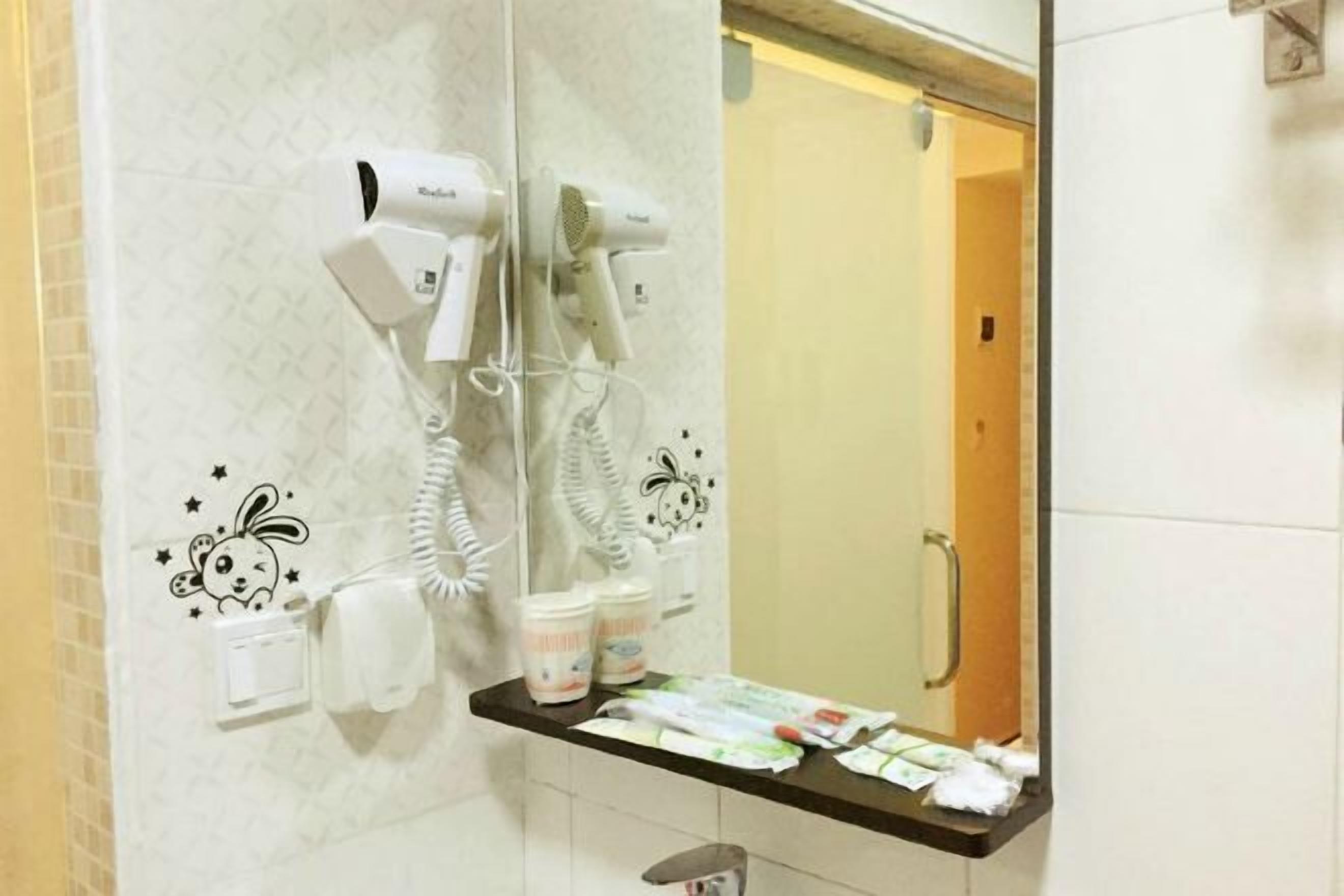 A bathroom with two hair dryers mounted on the wall, a mirror, and a countertop with toiletries.