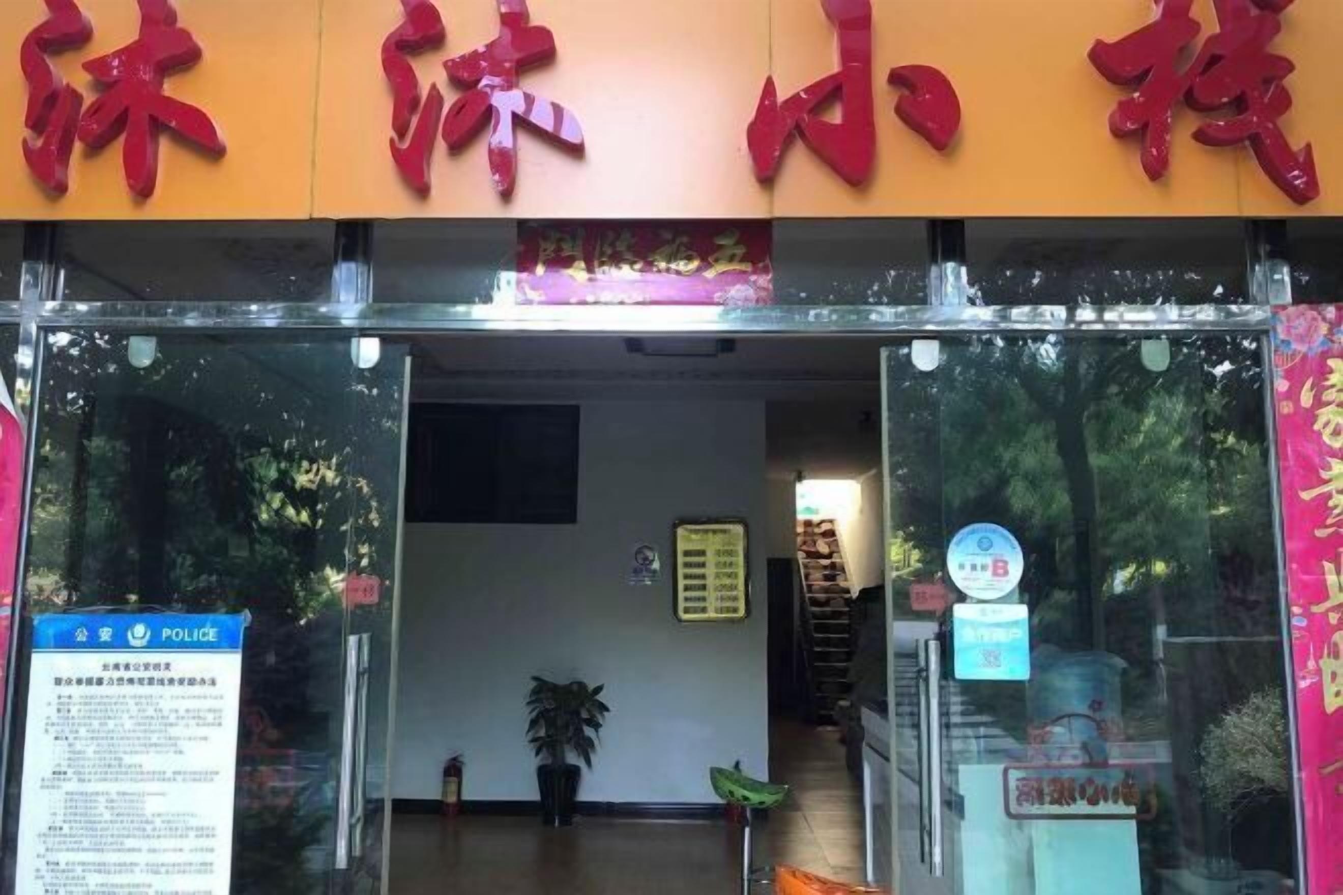 A hotel entrance with a red sign above the door, a blue police sign on the left, and a small potted plant inside.