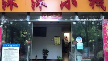 A hotel entrance with a red sign above the door, a blue police sign on the left, and a small potted plant inside.