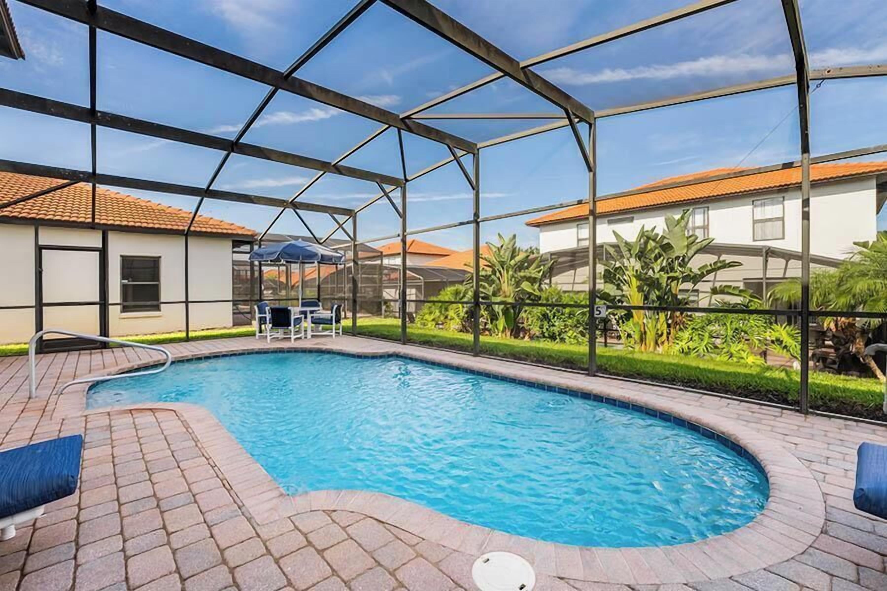 Ein Schwimmbecken mit Glasumrandung, umgeben von einer gepflasterten Terrasse und einer Grünfläche mit Pflanzen.