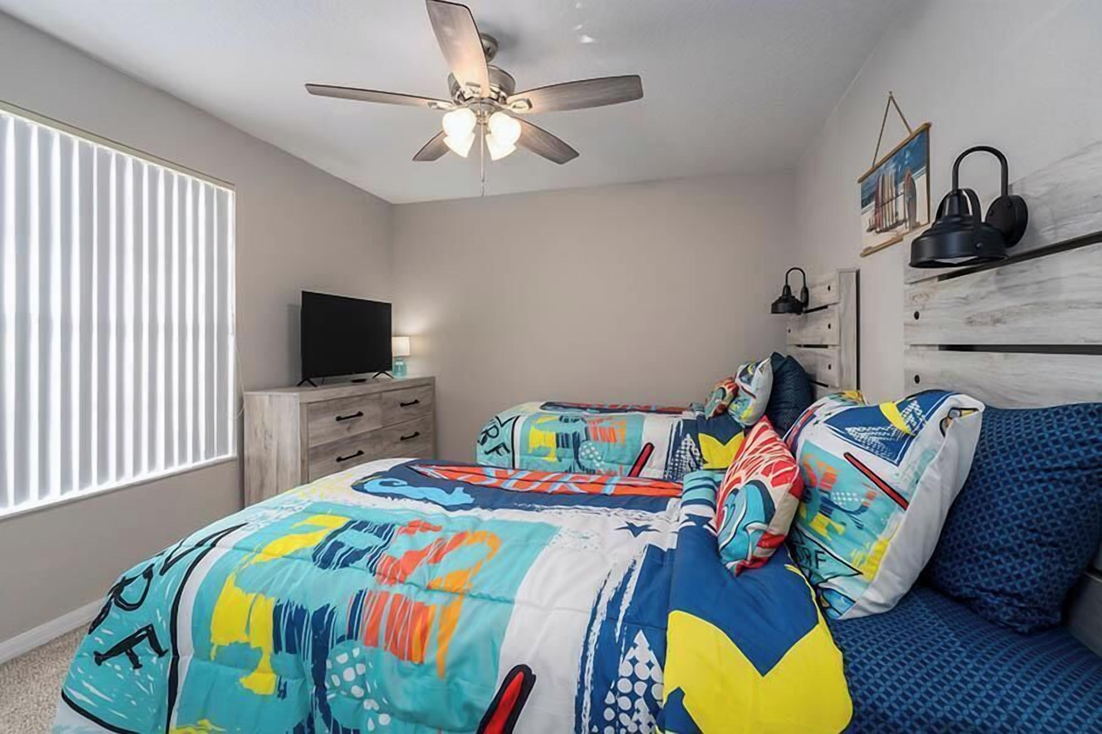 A bedroom with a bed, a ceiling fan, a TV, and a window with blinds.