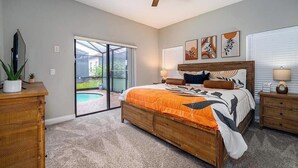 Een slaapkamer met een groot bed, een plafondventilator, een televisie, een schuifdeur naar een terras en kunst aan de muur.