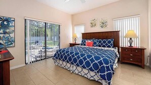 A bedroom with a large bed, two bedside tables with lamps, a ceiling fan, and a sliding glass door leading to an outdoor area. - Sandy Toes Hideaway - Private Pool & Games Room (Clermont)